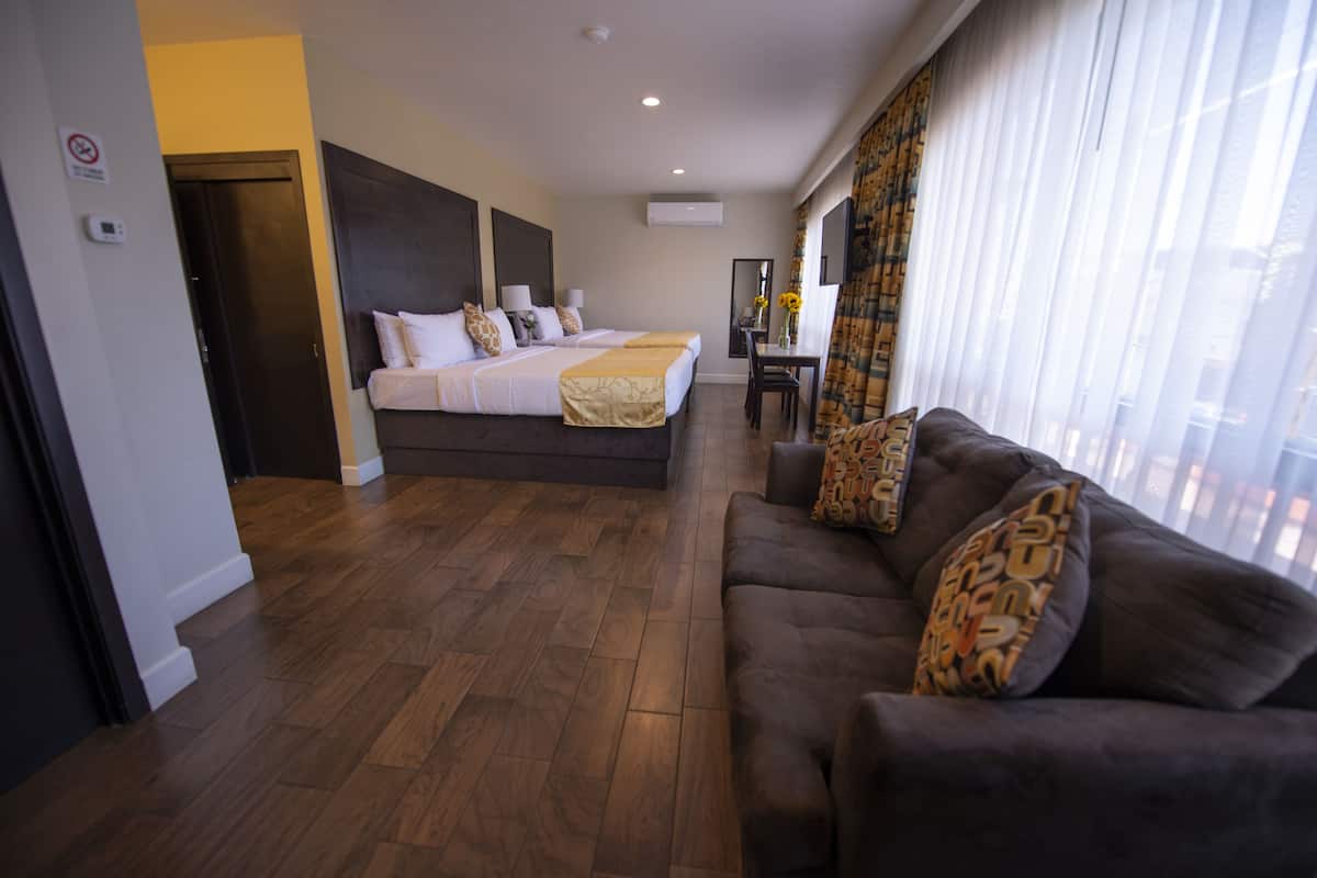 Une chambre d’hôtel avec un grand lit, un canapé, un bureau avec une chaise et une fenêtre avec des rideaux.