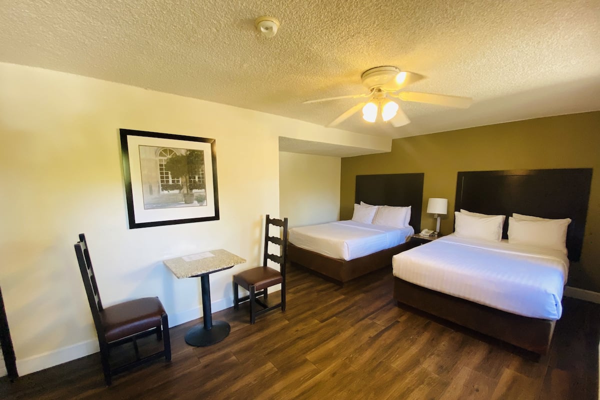 Une chambre d’hôtel avec deux lits, un bureau, une chaise et un ventilateur de plafond.