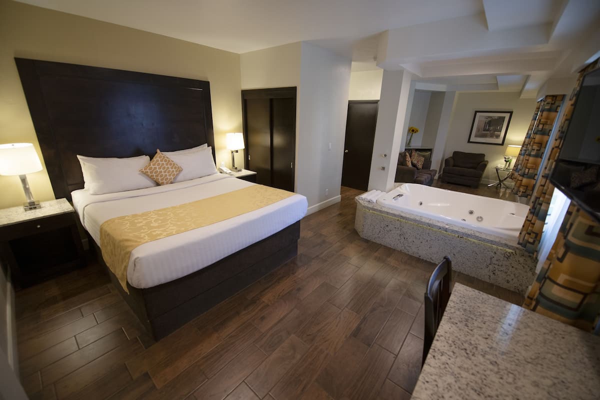 Une chambre d’hôtel dotée d’un grand lit, d’une salle de bain séparée avec un jacuzzi, d’un coin salon avec un fauteuil et une table, et d’une télévision.