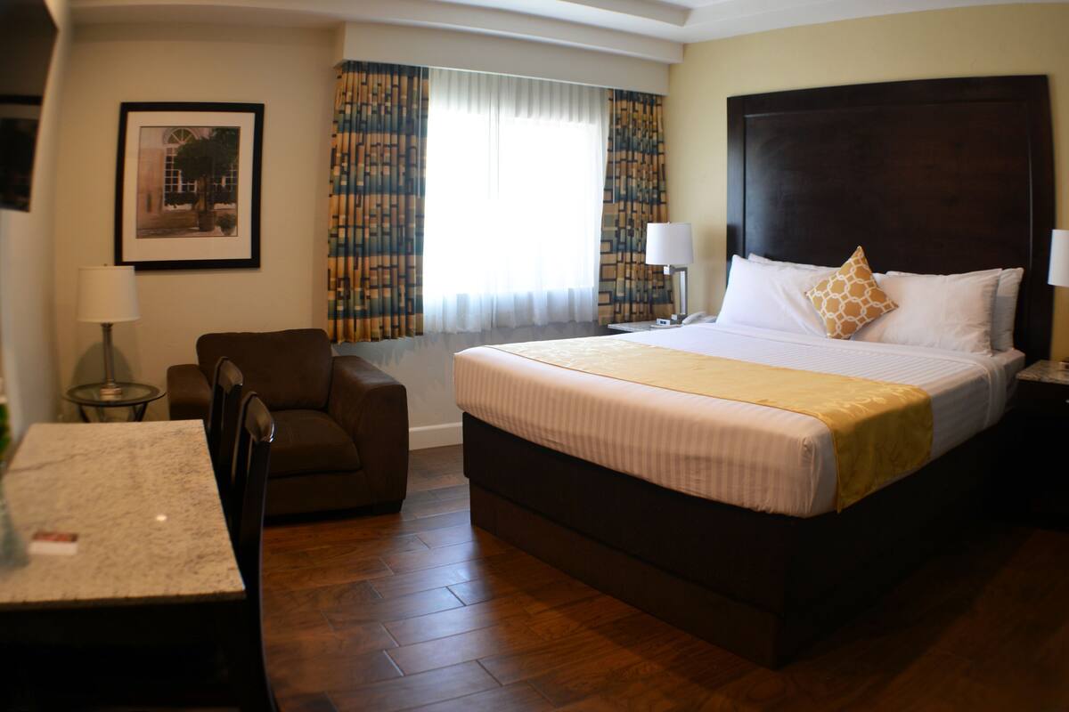Une chambre d’hôtel avec un grand lit, un bureau, une chaise et une fenêtre avec des rideaux.