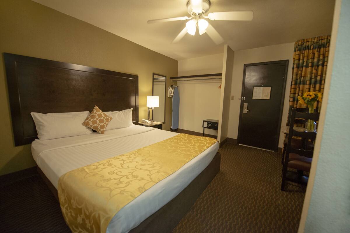 Une chambre d’hôtel avec un grand lit, un ventilateur de plafond, une table de chevet, une lampe, une porte et une chaise.