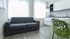 Eine moderne Küche mit weißen Schränken, einem grauen Sofa und einem grünen Sessel.
