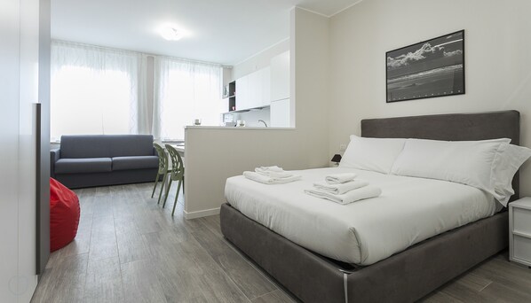 A modern hotel room with a bed, a sofa, a dining area, and a bathroom.
