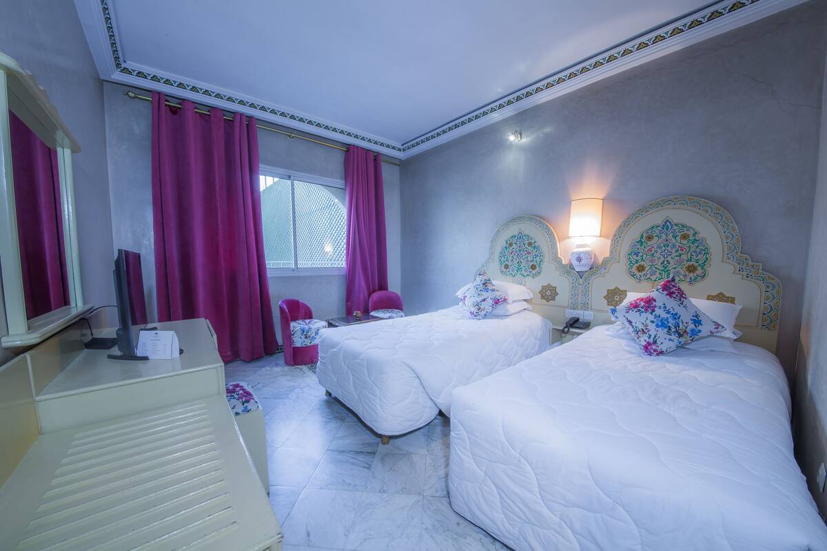 A hotel room with two beds, a desk, a chair, and a window with curtains.