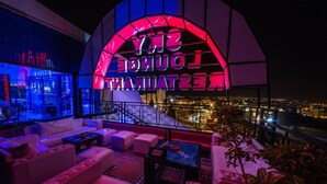 Un área de lounge en la azotea con un letrero de neón que dice "SNY LOUNGE" y vistas de la ciudad.