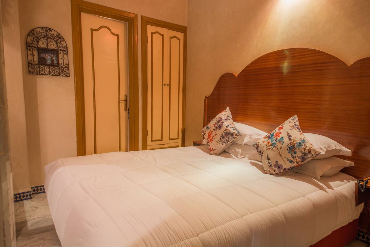 A neatly made bed with white bedding and floral pillows, a wooden headboard, and a door with a decorative frame.