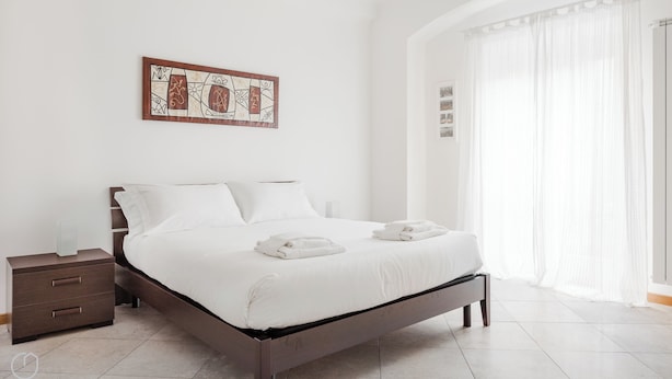 Quarto moderno com cama, mesa de cabeceira e obra de arte na parede.