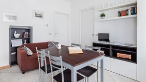 Um espaço de estar moderno com uma mesa de jantar, cadeiras, um sofá, uma estante e uma televisão.