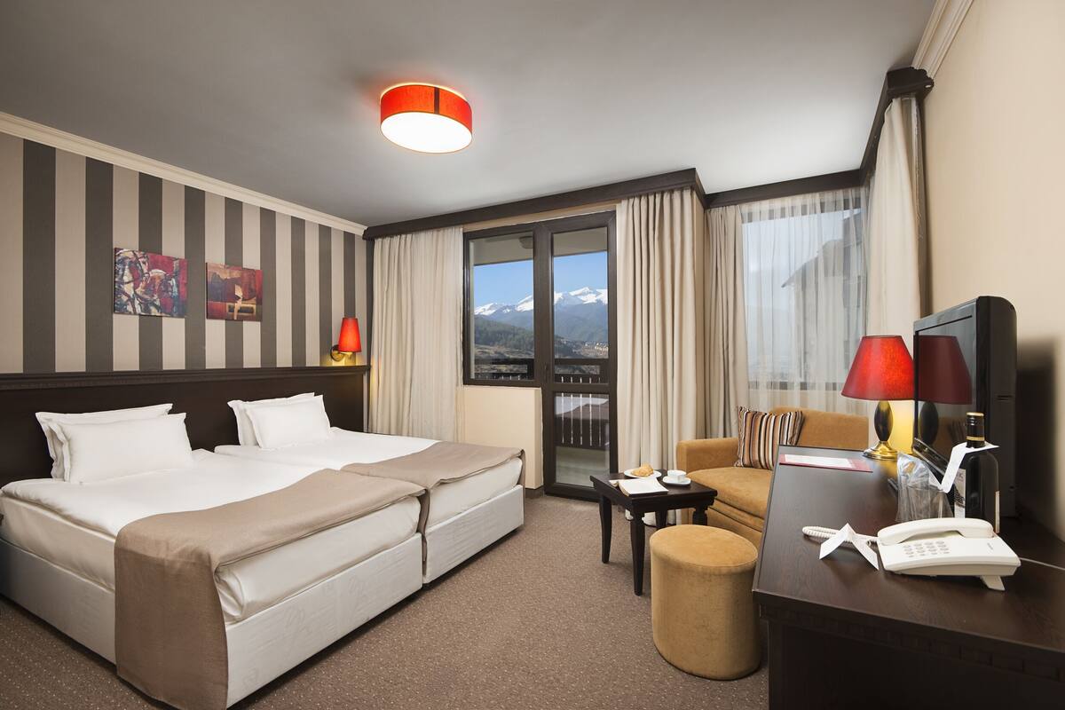 Quarto de hotel com uma cama, escrivaninha, cadeira, mesa, abajur, telefone e vista para as montanhas.