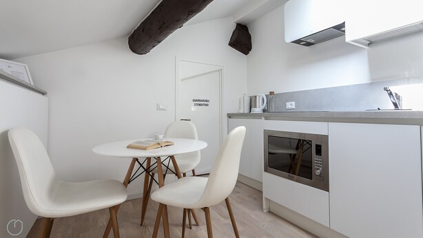 Eine moderne Küche mit weißen Schränken, einem eingebauten Backofen und einem Essbereich mit einem runden Tisch und weißen Stühlen.