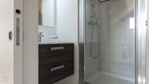 Ein modernes Badezimmer mit einer Duschkabine aus Glas, einem dunklen Holzwaschtisch und einem Spiegel über dem Waschbecken.
