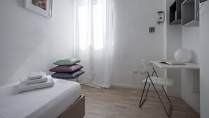 Ein modernes, minimalistisches Schlafzimmer mit Bett, Stuhl und Schreibtisch.