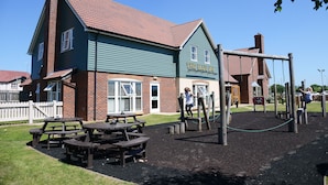 A playground with climbing structures and picnic tables in front of a building with a sign reading "The Blue Jay".