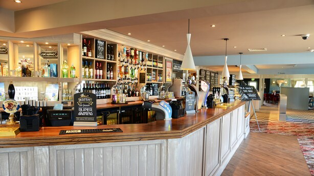 A bar area with a wooden counter, shelves of liquor bottles, and a sign indicating a special offer.