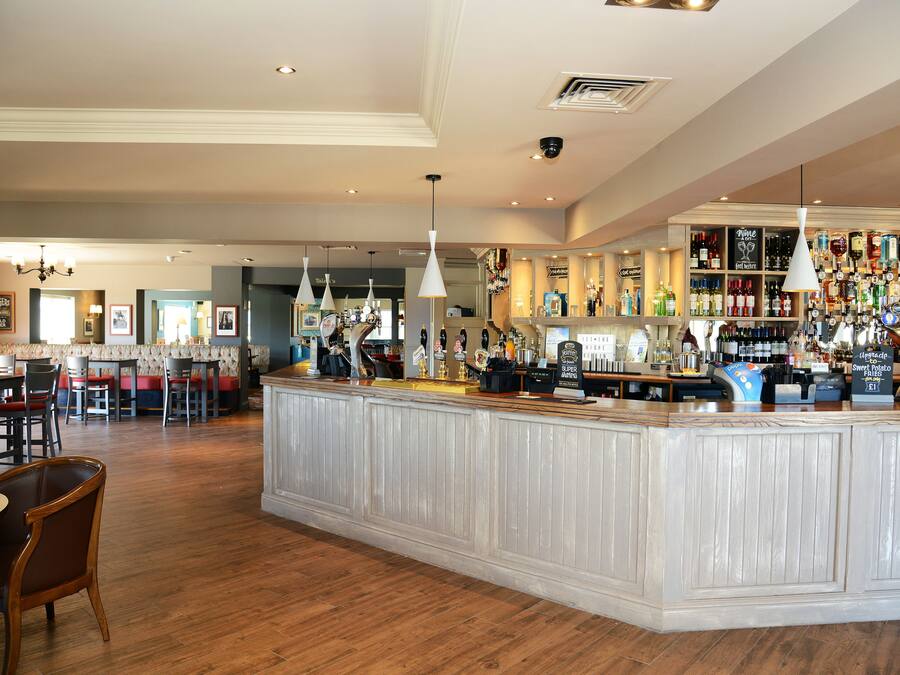 Una zona de bar con mostrador de madera, luces colgantes y una variedad de botellas y vasos.
