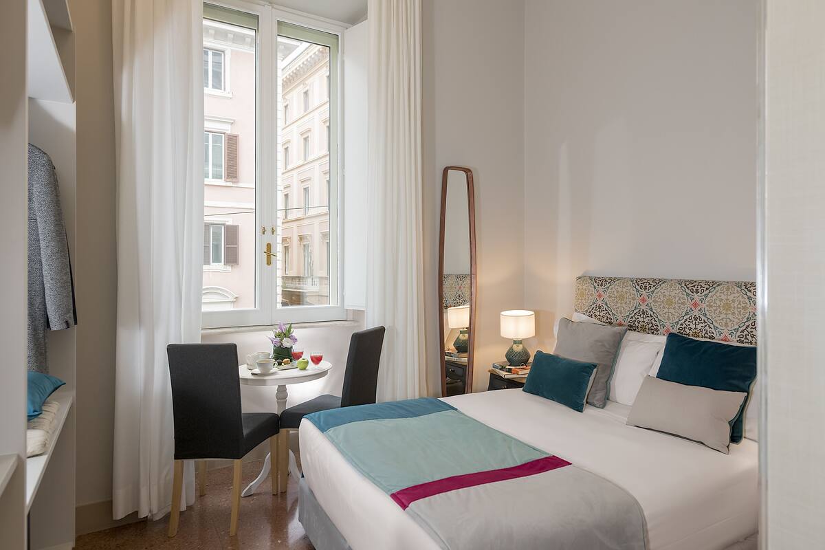Habitación de hotel con cama, escritorio, silla, espejo y ventana con vistas a edificios.