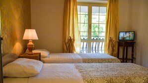 Habitación de hotel con dos camas, una lámpara, un televisor y un ventanal con cortinas.