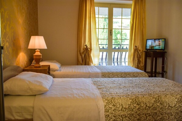 A hotel room with two beds, a lamp, a television, and a window with curtains.