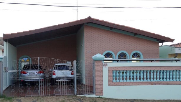 A two-story house with a gated driveway, a covered carport, and a decorative wall with arched windows. - Pousada Santa Genebra (Campinas)