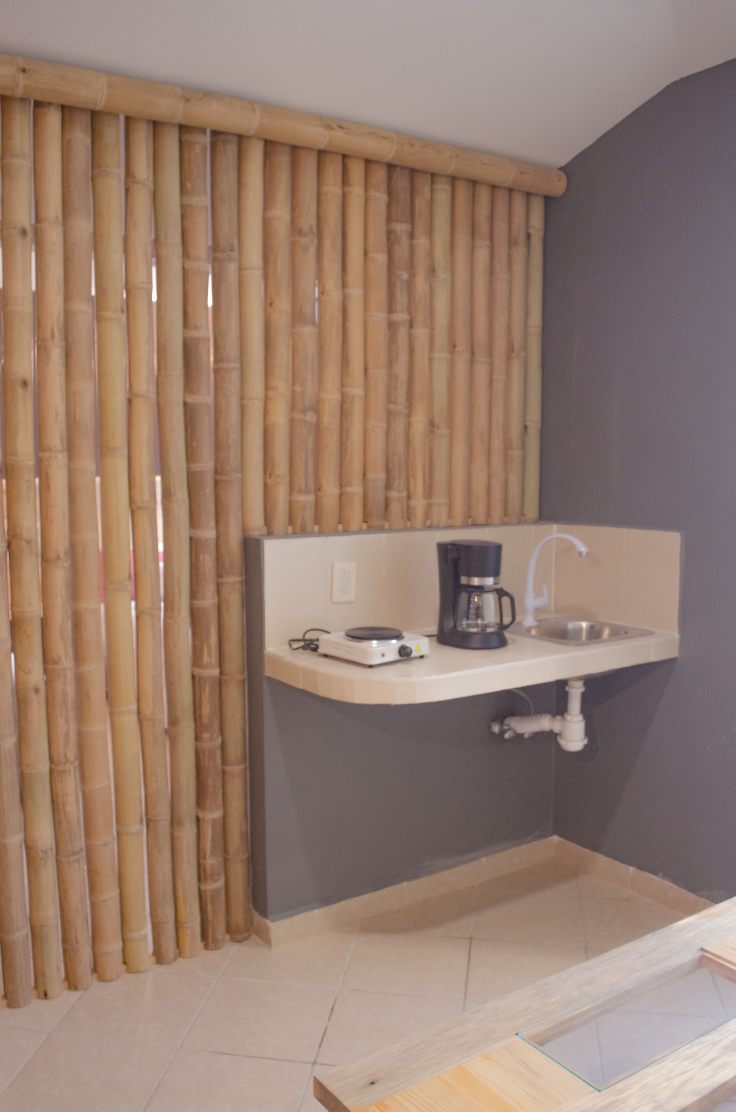 Un baño con separador de bambú, un lavabo con grifo, una cafetera y una pequeña encimera.