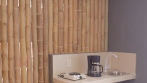 Ein Badezimmer mit Bambusabtrennung, einem Waschbecken mit Wasserhahn, einer Kaffeemaschine und einer kleinen Ablagefläche.