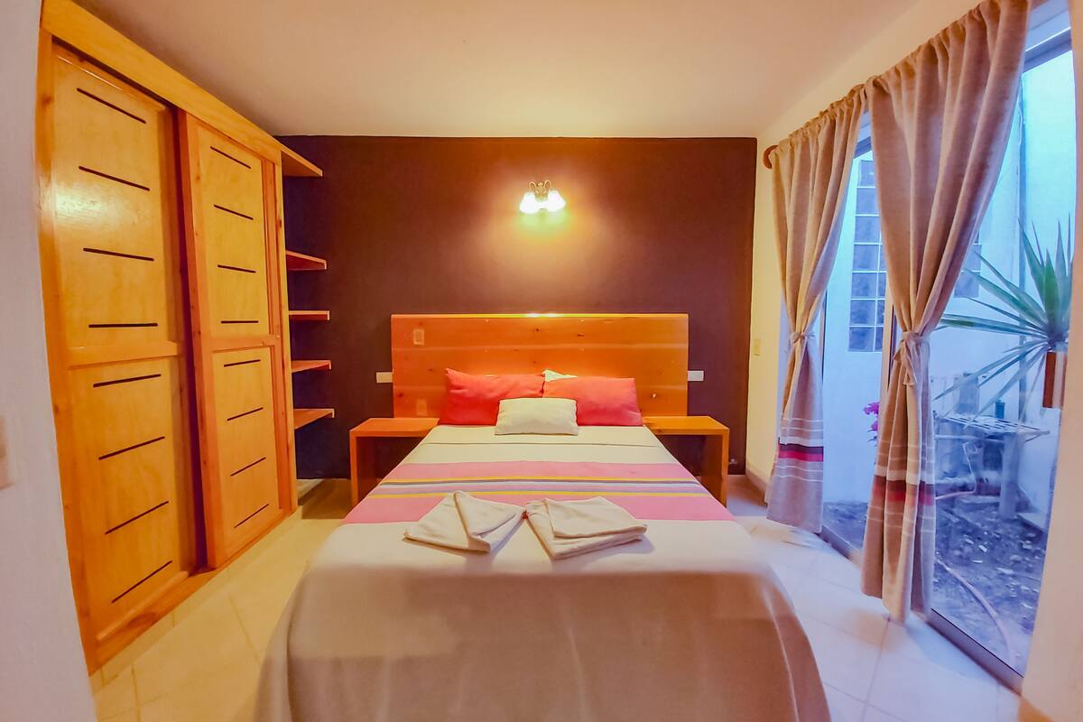 Een slaapkamer met een bed, een houten kledingkast, nachtkastjes en een raam met gordijnen.