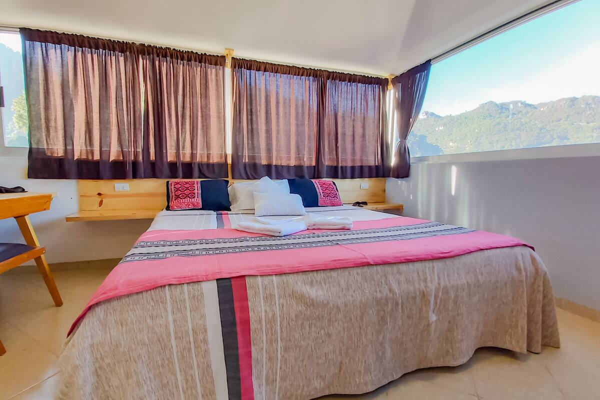 Een keurig opgemaakt slaapkamer met een groot bed, een houten bureau en een raam met gordijnen.