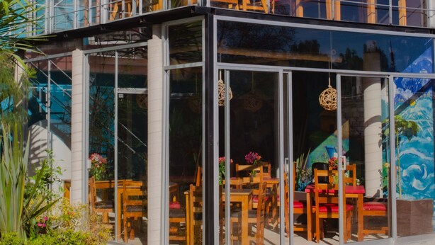 Ein modernes Gebäude mit Glasfassade, Außenbereich mit Sitzgelegenheiten und einem sichtbaren Balkon.