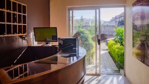 Ein Empfangsschalter mit Computer, Schlüsseln an einem wandmontierten Träger und Blick auf einen Garten und Gebäude durch eine Glastür.