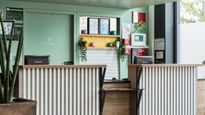 A reception area with a green wall, two reception desks, a wooden counter, and a small window.