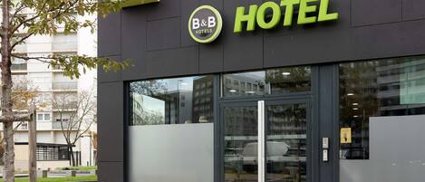 Un hotel moderno con fachada de vidrio, un logotipo llamativo de B&B Hotels y una entrada despejada.