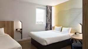 A hotel room with a large bed, a smaller bed, a desk, and a window with curtains.