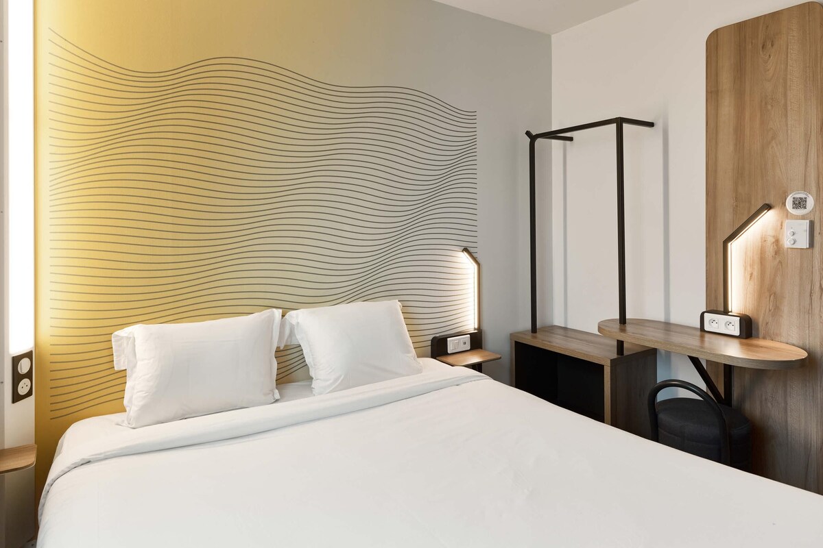 A modern hotel room with a bed, bedside tables, a desk, and a unique wavy wall design.