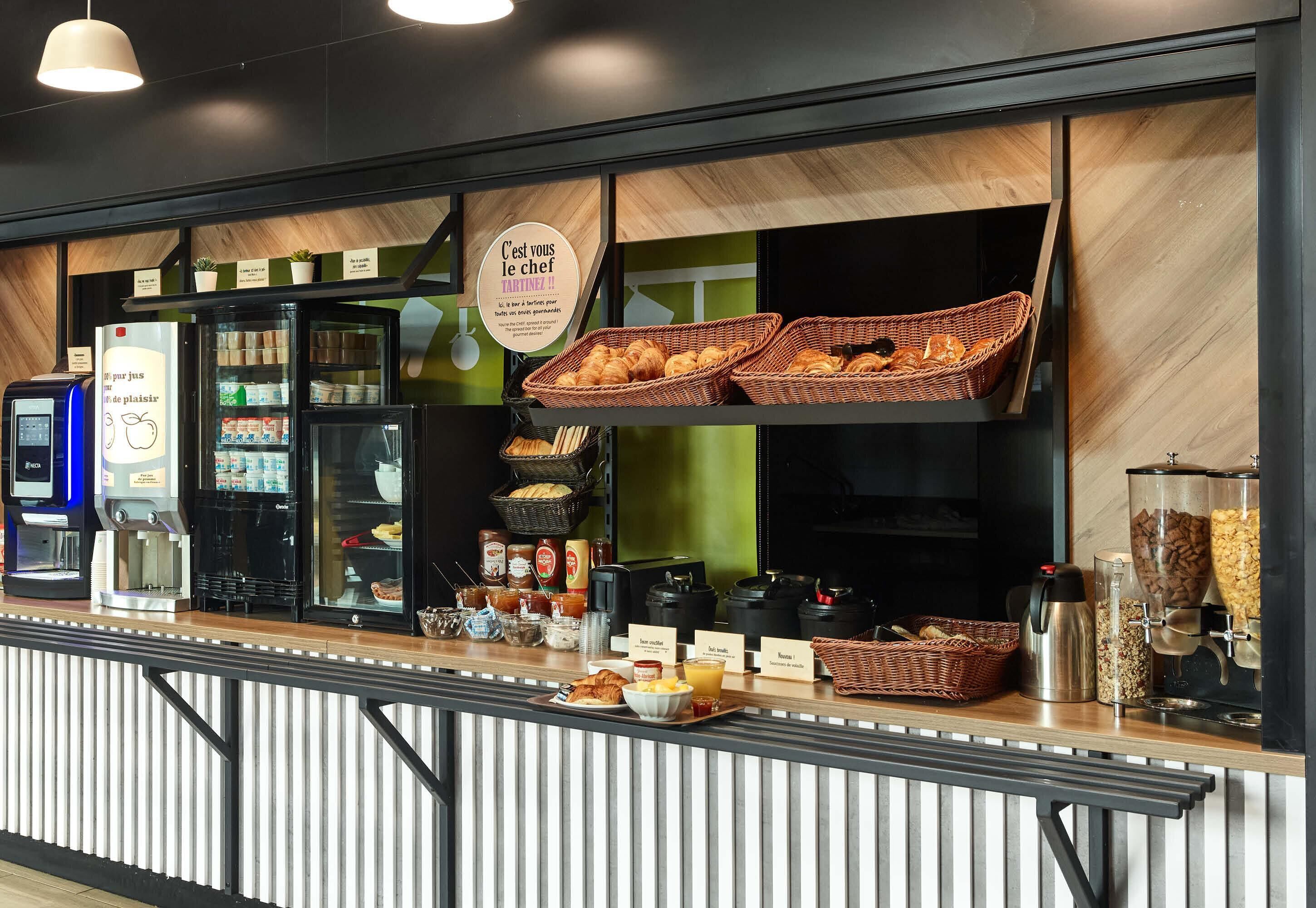 Un buffet per la colazione con cestini di pasticceria, macchine da caffè e un cartello con su scritto 'C'est vous le chef'.