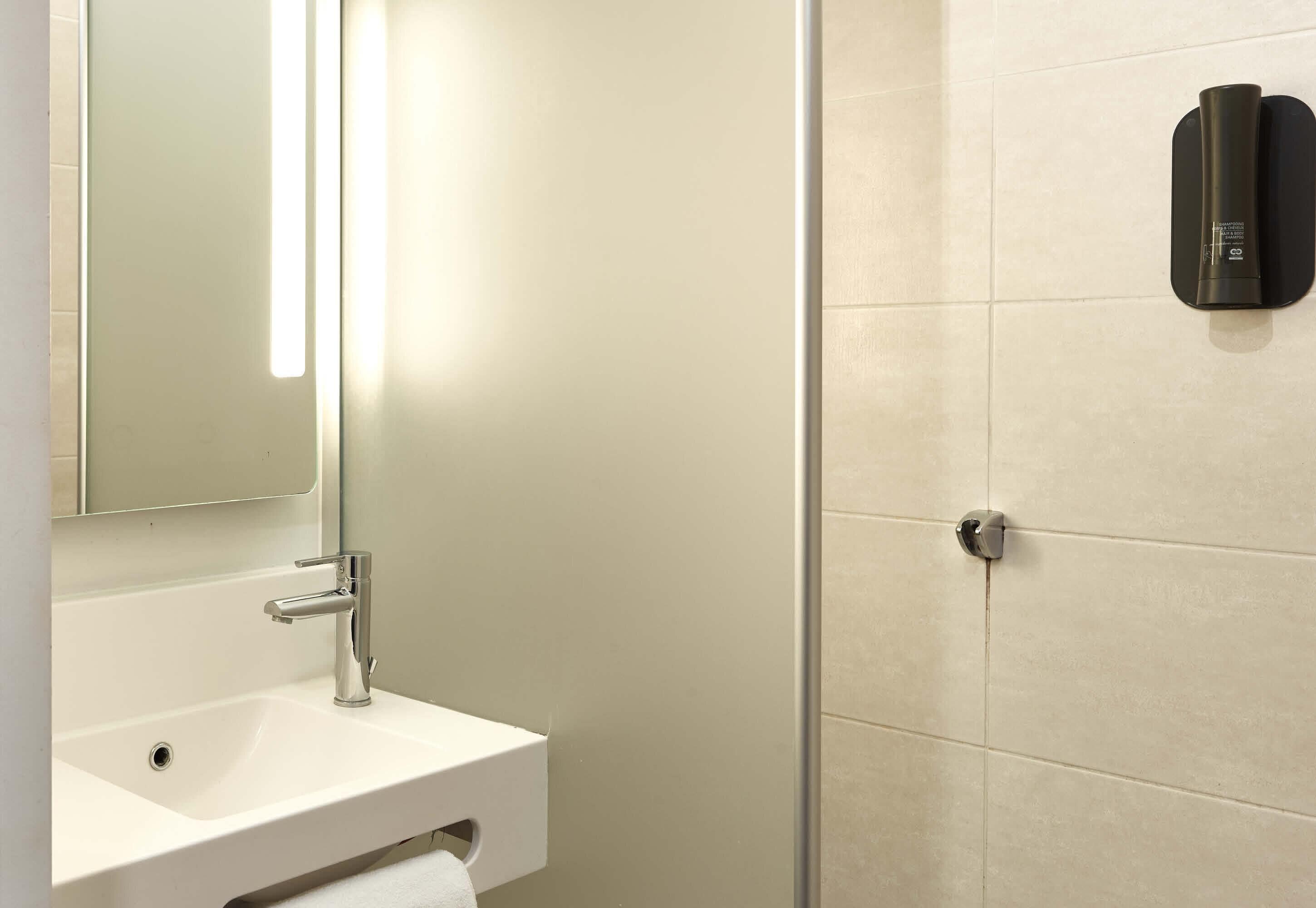 Baño con lavamanos blanco, espejo y zona de ducha.
