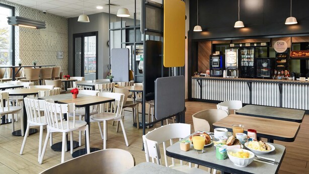 A modern cafe with multiple seating areas, including tables and chairs, and a counter with food and drink options.