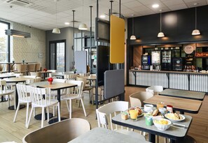 A modern cafe with multiple seating areas, including tables and chairs, and a counter with food and drink options. - B&B HOTEL PARIS Gennevilliers Asnières (Gennevilliers)