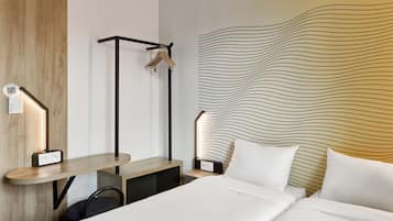 Habitación de hotel con cama, mesitas de noche, un escritorio, perchero y una pared con diseño ondulado.