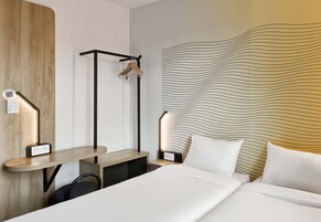 Habitación de hotel con cama, mesitas de noche, un escritorio, perchero y una pared con diseño ondulado.