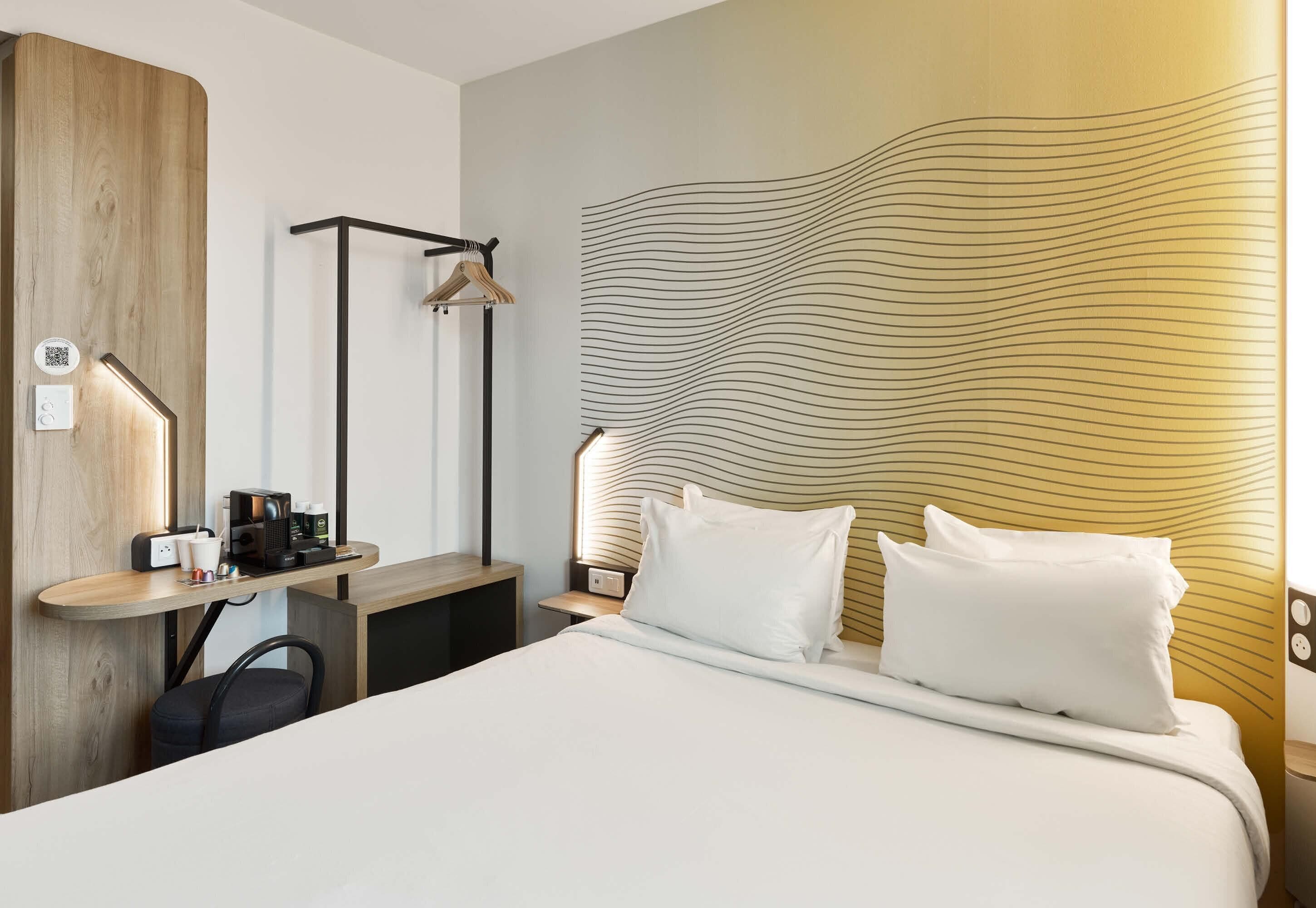 Una habitación de hotel con una cama, mesita de noche, lámpara y un papel tapiz con diseño ondulado.