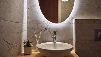 A bathroom with a marble wall, a wooden countertop, a white sink, a mirror, and a small potted plant.