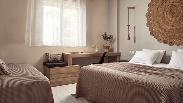 A bedroom with two beds, a bedside table, a nightstand, a window with sheer curtains, a woven wall hanging, and a small potted plant. - Casa Del Mar (Zakynthos)