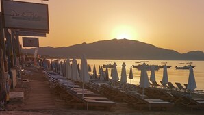 A beachside view with sunlit mountains, a row of sun loungers, and a calm sea. - Casa Del Mar (Zakynthos)