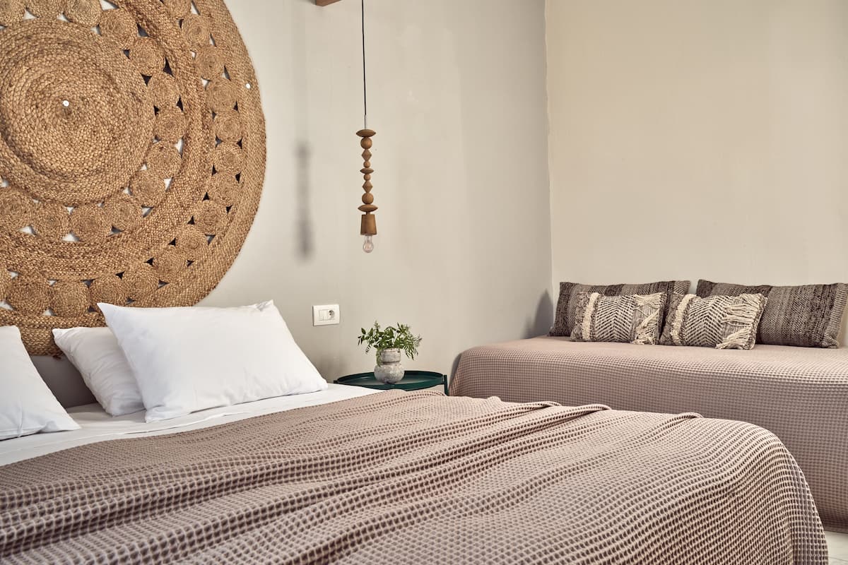 A bedroom with two beds, a large woven headboard, a hanging light fixture, and a small plant on a nightstand.
