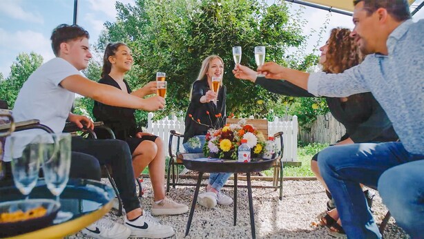 Um grupo de pessoas brindando com bebidas ao redor de uma mesa com um arranjo floral.