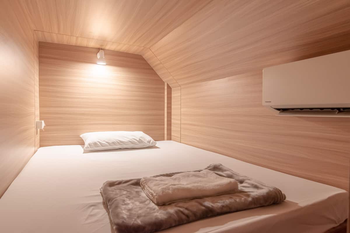 A bedroom with a sloped ceiling, a bed with white bedding, a brown throw blanket, and a wall-mounted air conditioner.