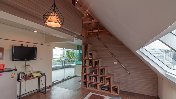 A modern living space with a kitchen area, a wooden staircase, and a skylight. - The Victory View - Hostel - Adults only (Bangkok)