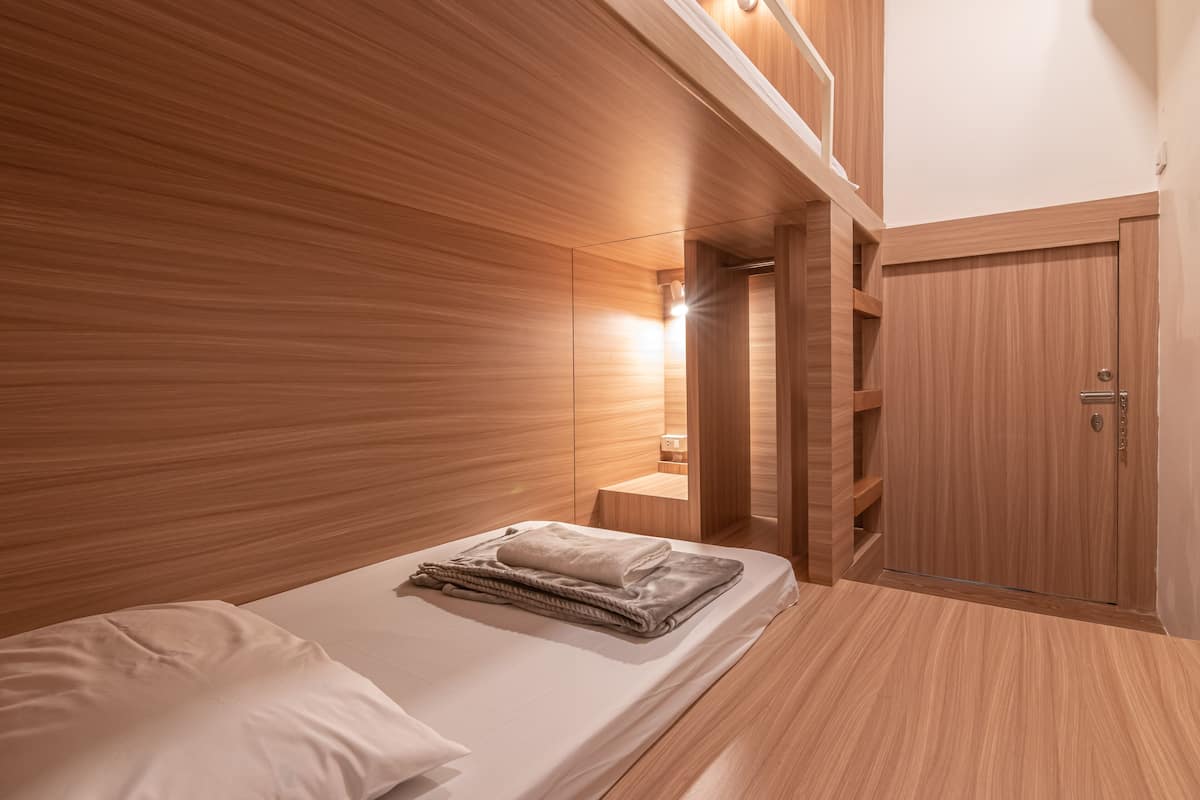 A modern bedroom with a wooden headboard, a neatly made bed with a folded blanket, and a wooden wardrobe.