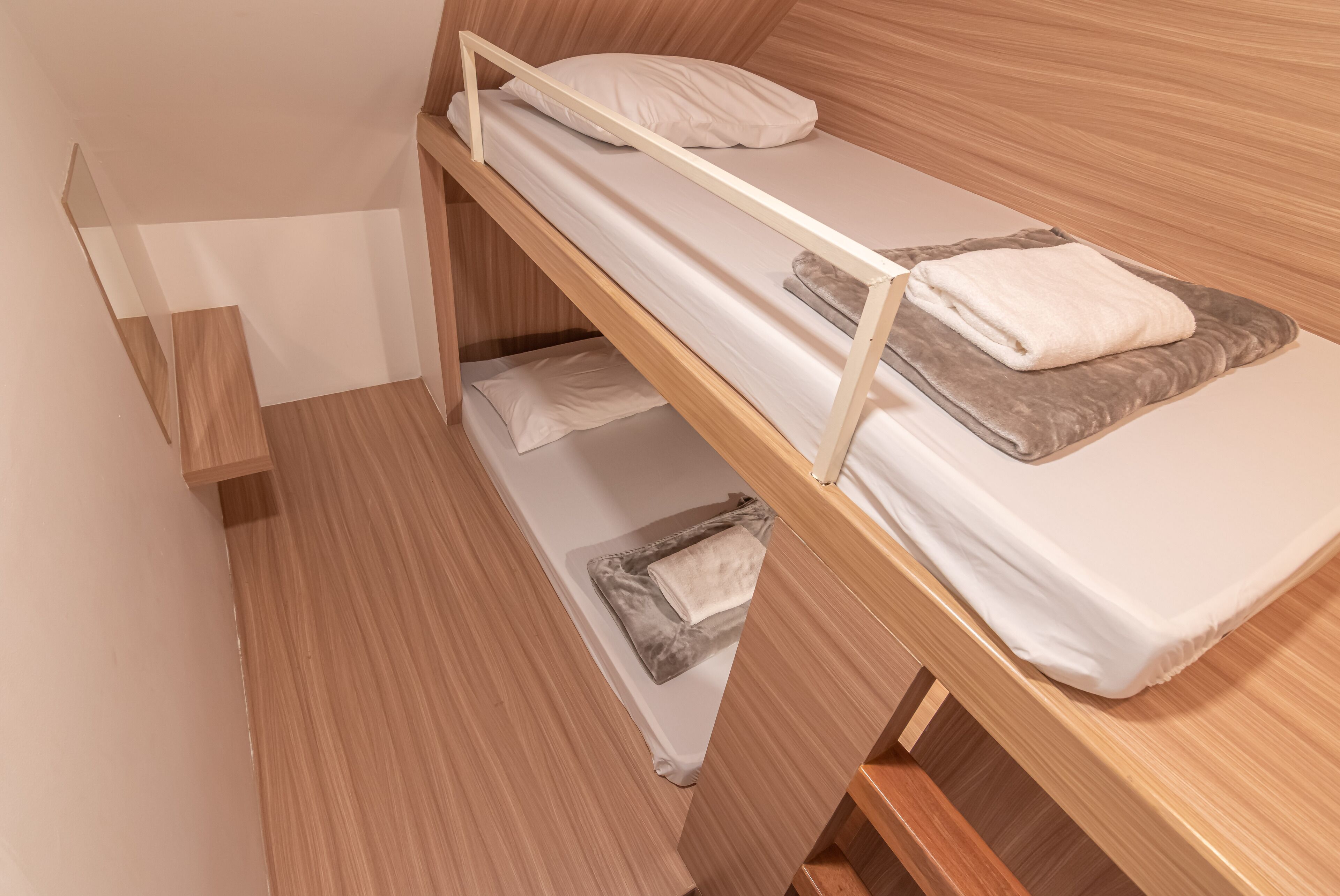 Una cama individual en literas con ropa de cama blanca y una manta gris.