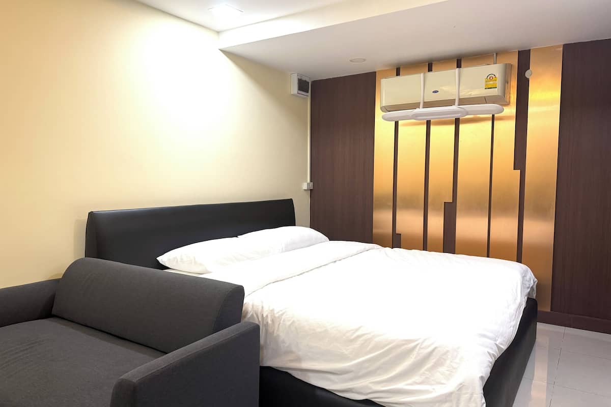 A hotel room with a bed, a sofa, and an air conditioning unit on the wall.